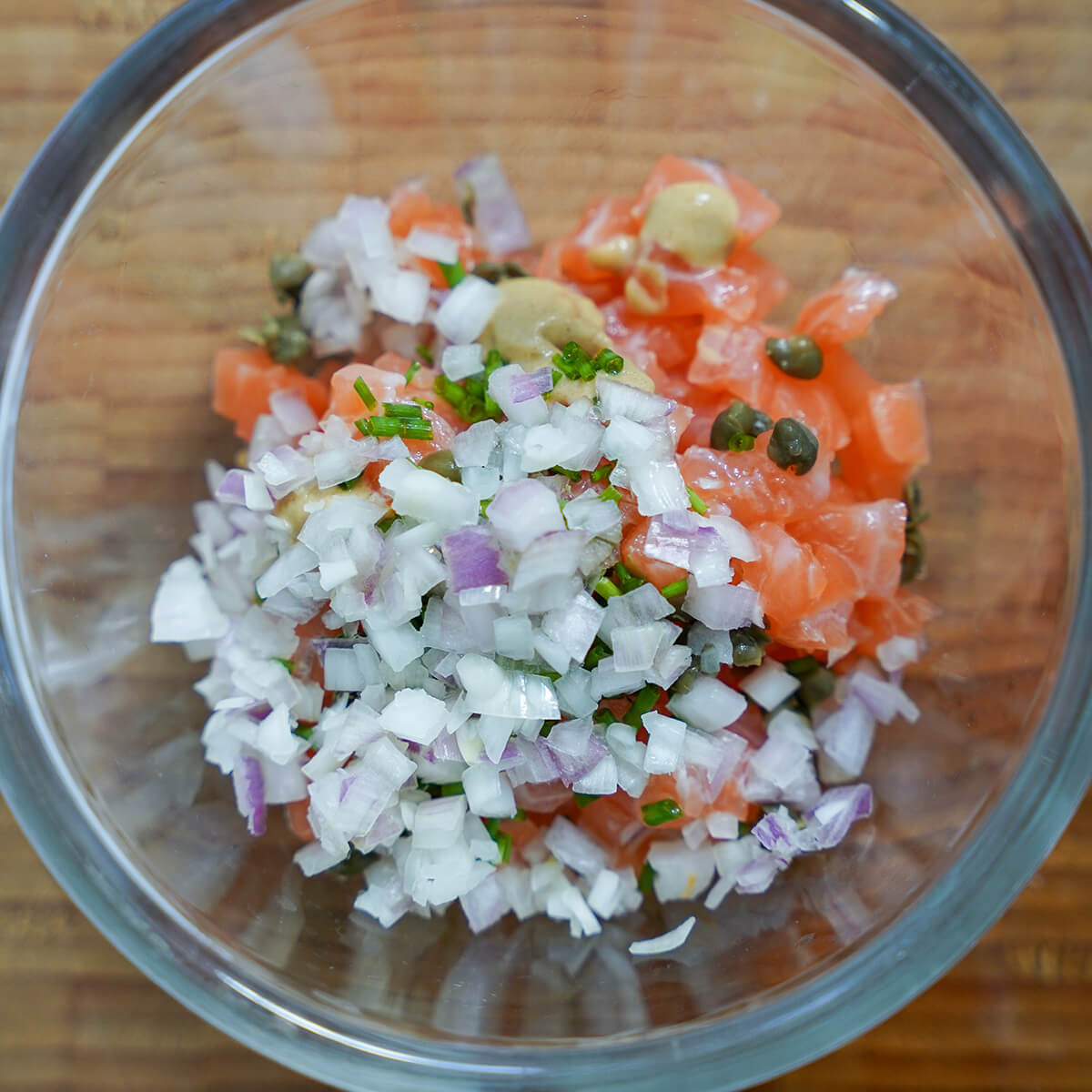 bowl with diced shallots over diced salmon, mustard, capers and chopped chives showing through.