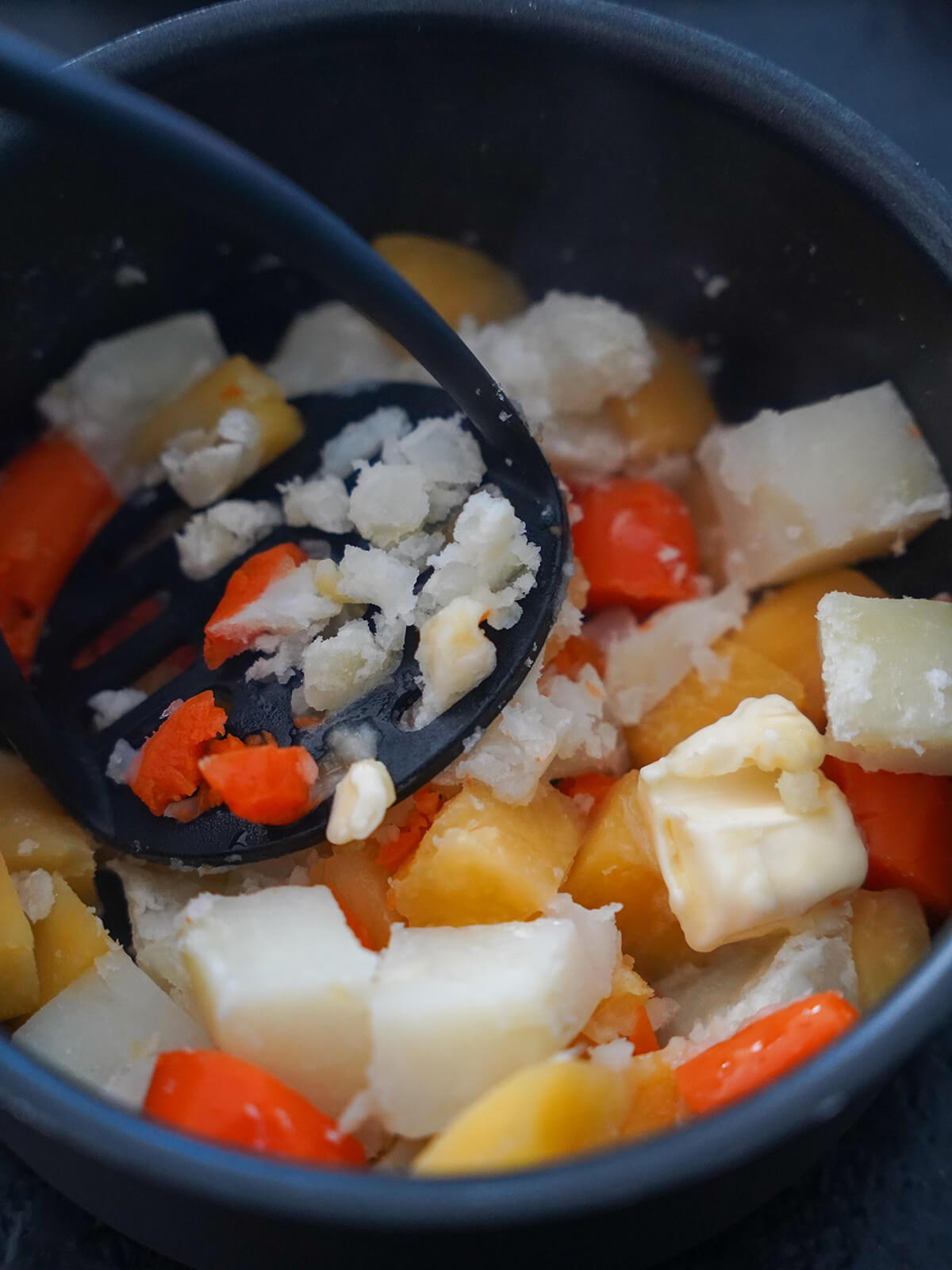 mashing vegetables and butter together in pot.