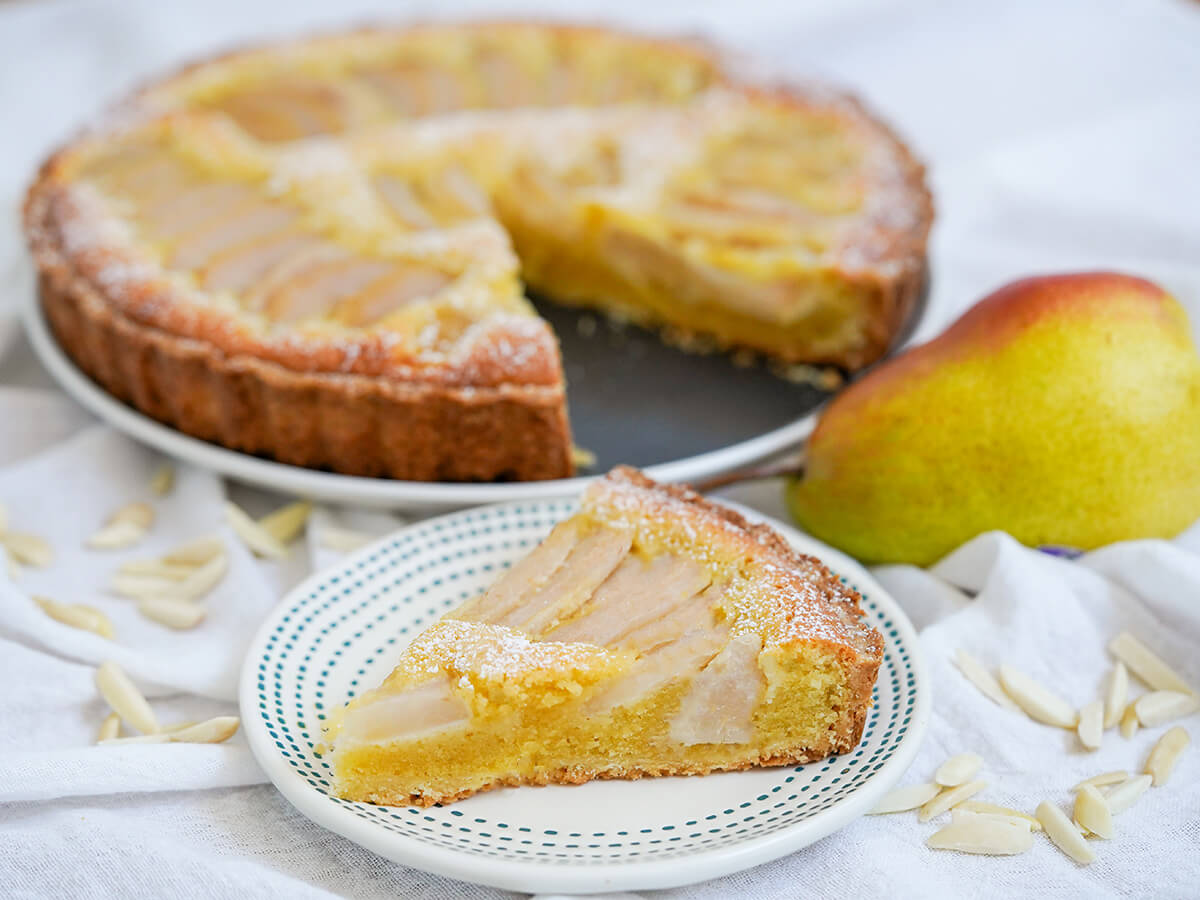 slice of pear frangipane tart with cranberries, a delicious treat any time slice of pear frangipane tart on small plate in front of pear and rest of tart.
