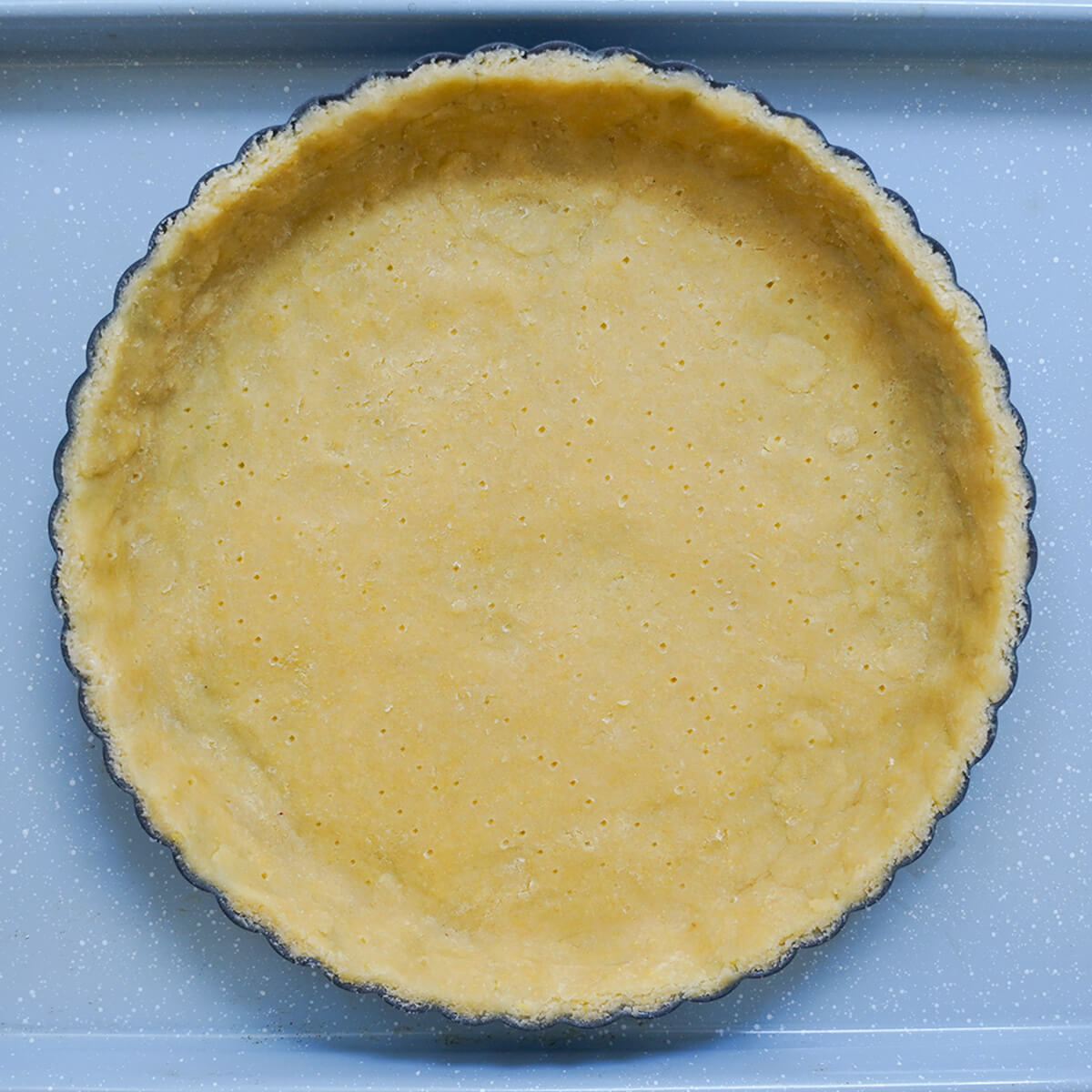 pastry in tart pan with surface pricked before being baked.