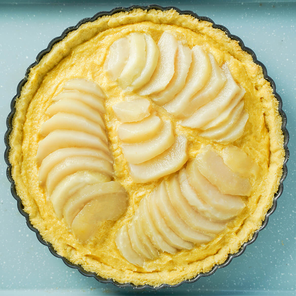 nestling slices of pear into frangipane base for pear frangipane tart sliced pears in frangipane mixture inside pastry shell before baking.