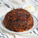 whole Christmas pudding on plate with brandy butter blurred in backgorund.