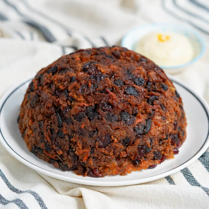 whole Christmas pudding on plate with brandy butter blurred in backgorund.