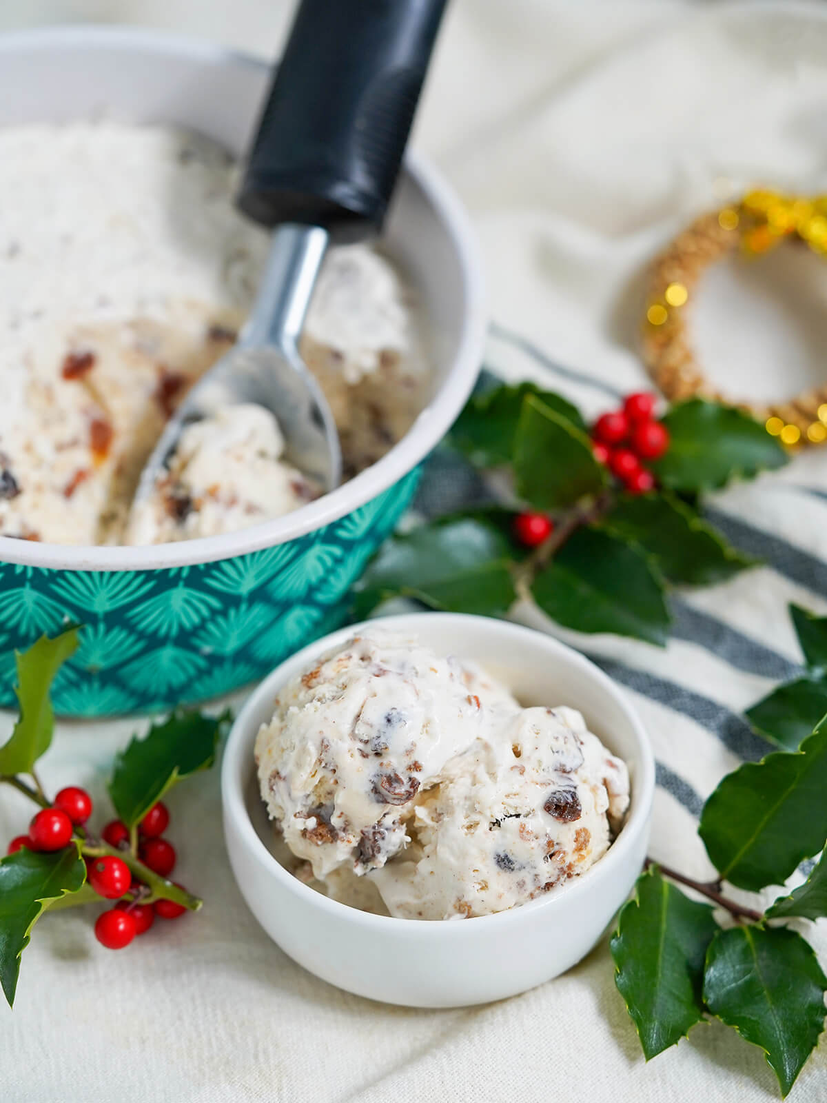 small bowl with scoops of Christmas pudding ice cream with scoop in dish behind and holly around.