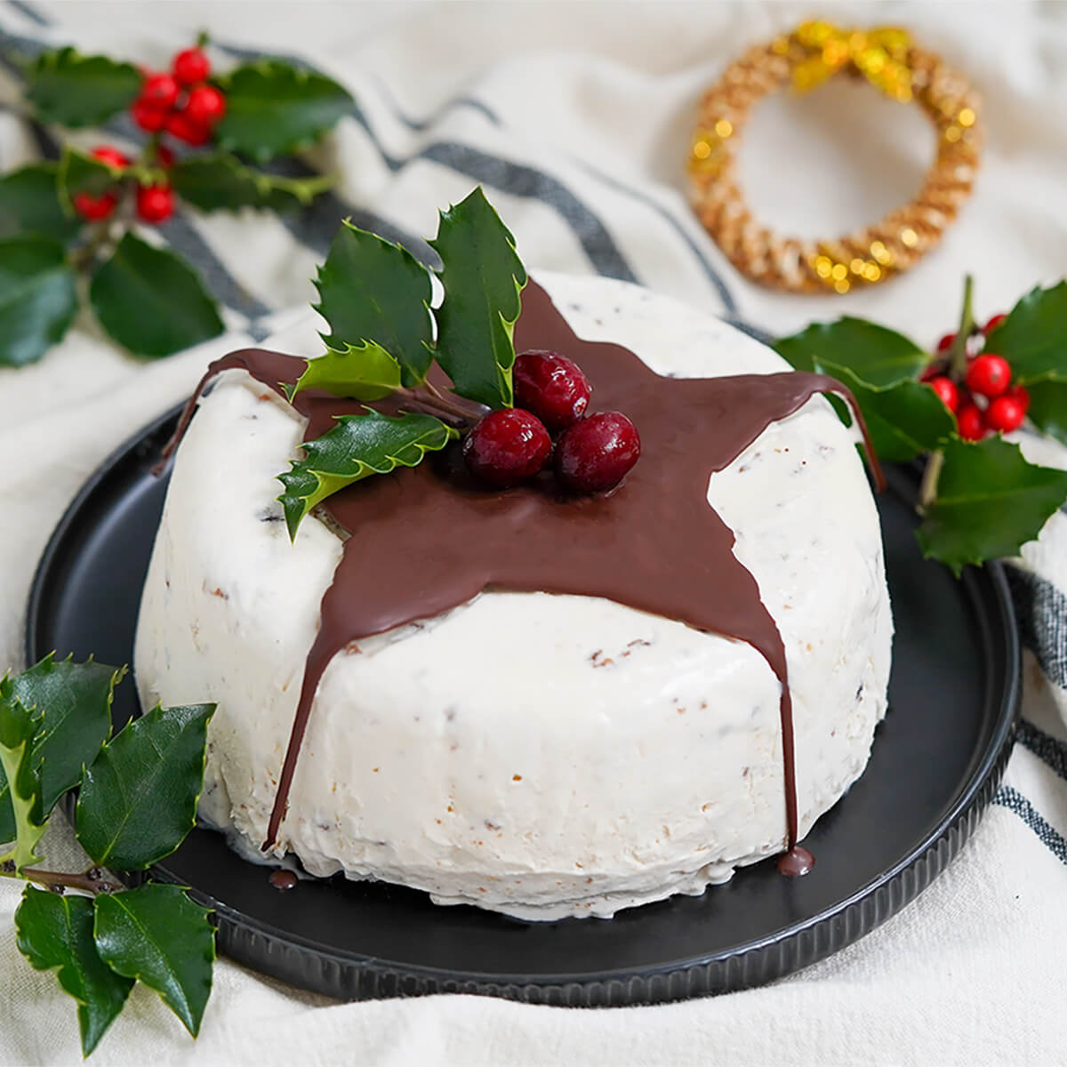 Christmas pudding ice cream decorated with chocolate drip, cranberries and holly.