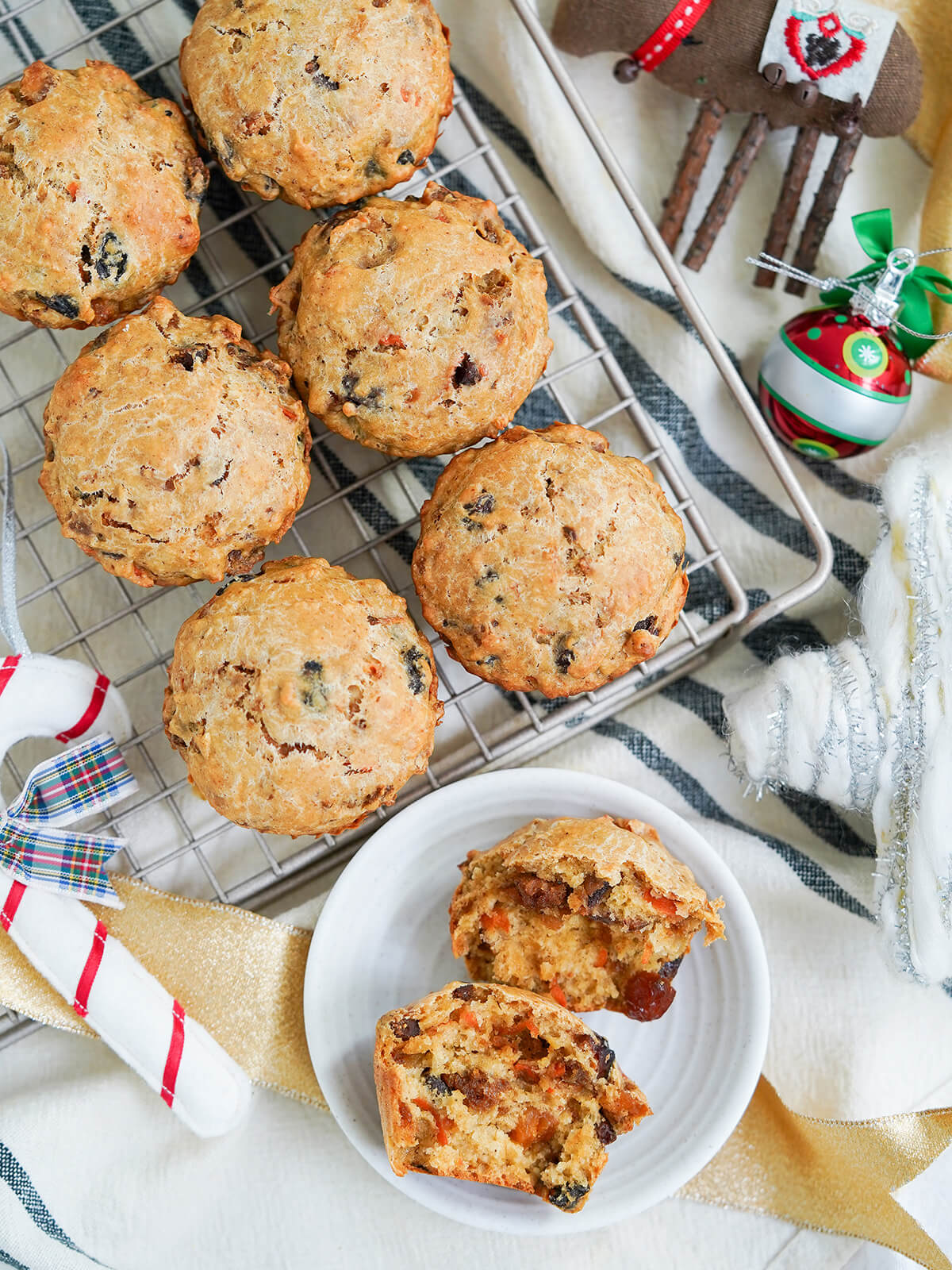 overhead view of Christmas pudding muffins on cooling rack with one split open on plate below with decorations around.
