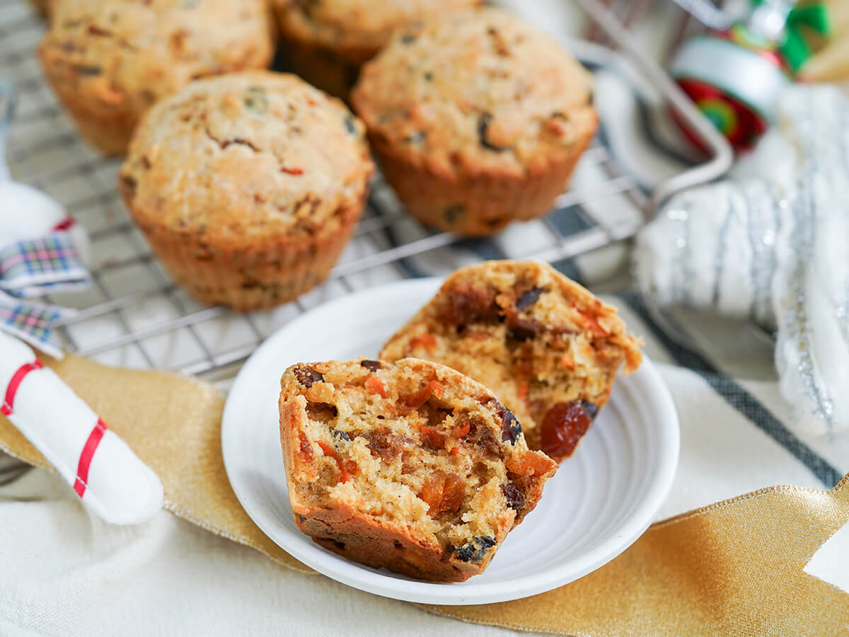 Christmas pudding muffins with one split open on plate in front of more blurred in background behind.