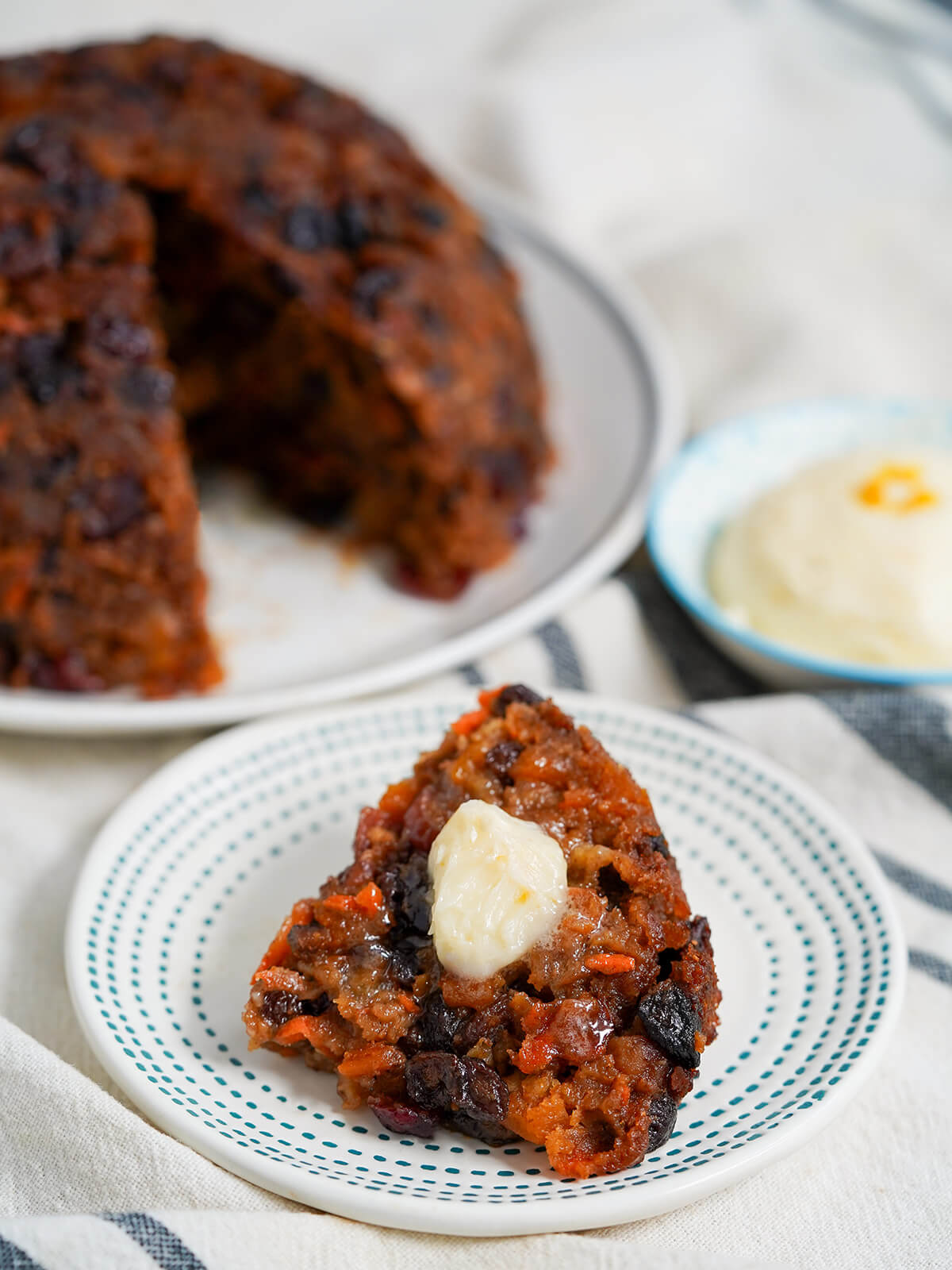 slice of Christmas pudding topped with brandy butter with rest on plate behind.