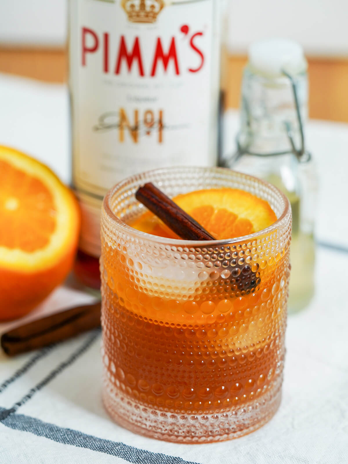 side view of glass of Winter Pimms cup with bottles blurred in background.