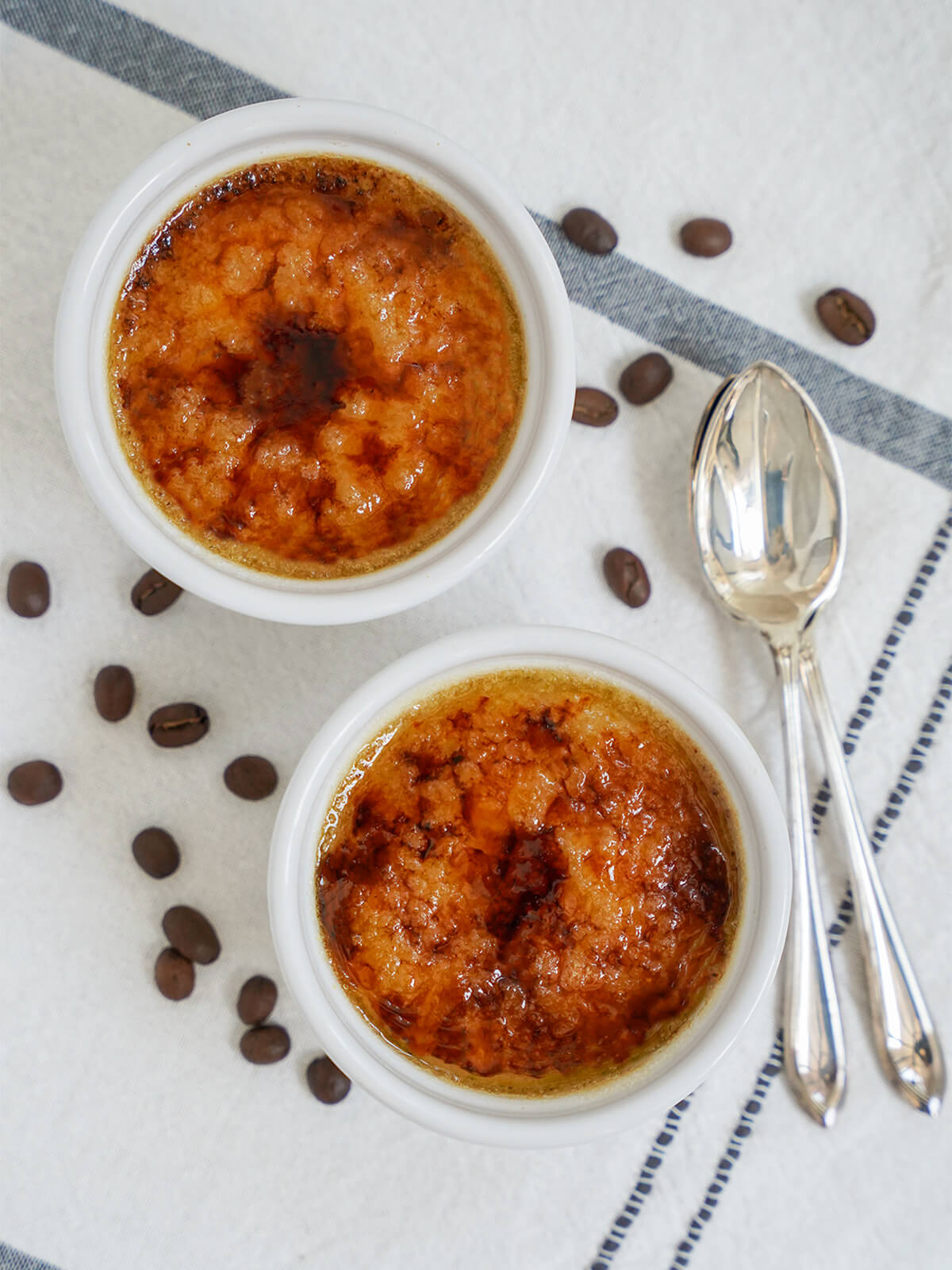 two dishes of coffee creme brulee from overhead with spoons to side.
