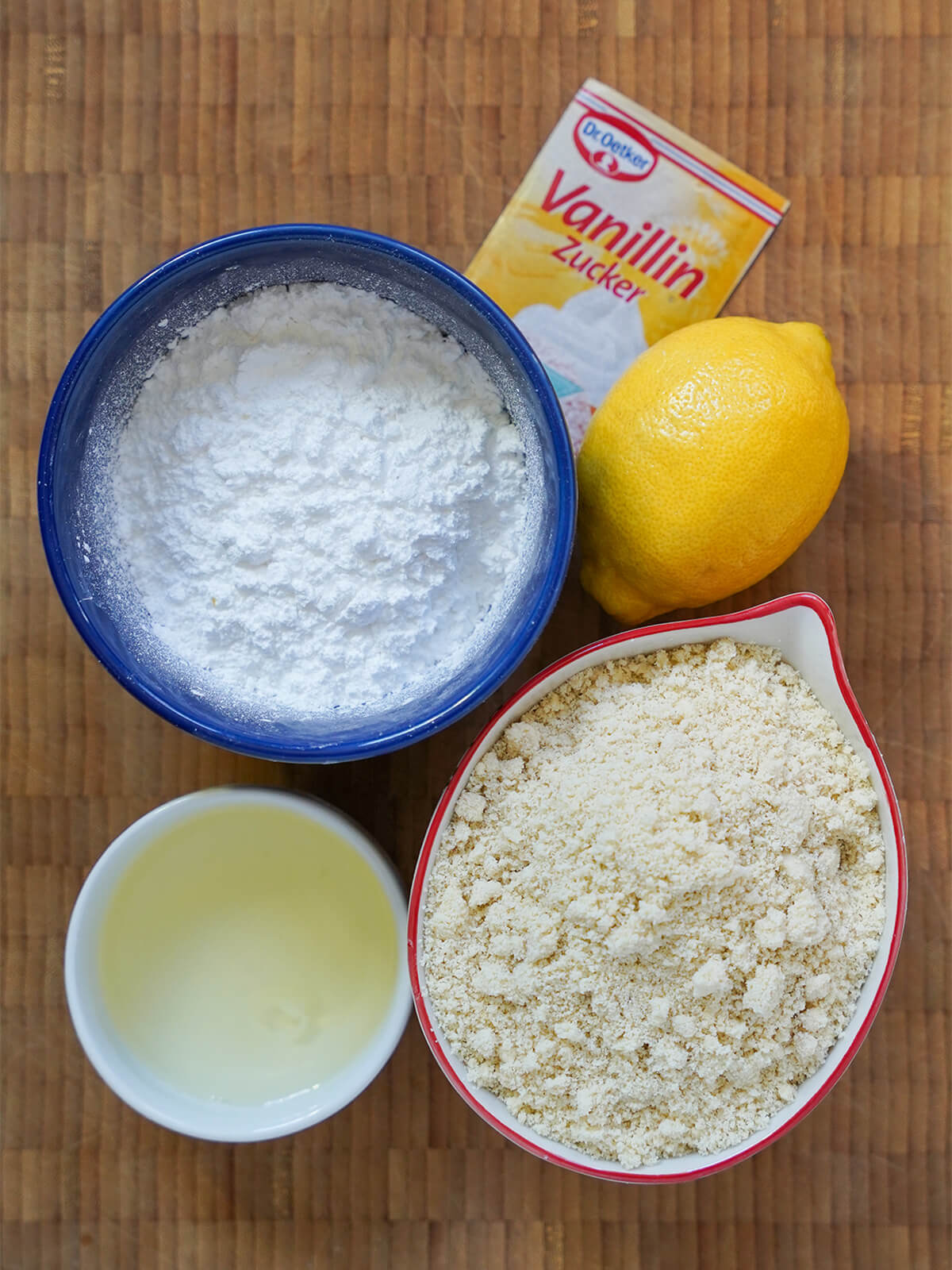 bowl of powdered sugar, another of ground almonds, small dish of egg white and lemon, vanilla sugar packet above.