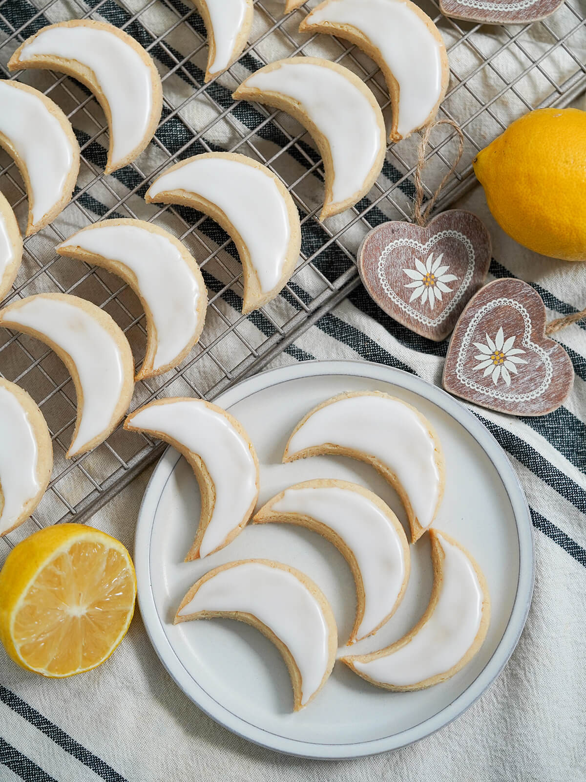 overhead view of plate of lemon almond cookies zedernbrot with more on cooling rack to side and lemons to wither side.