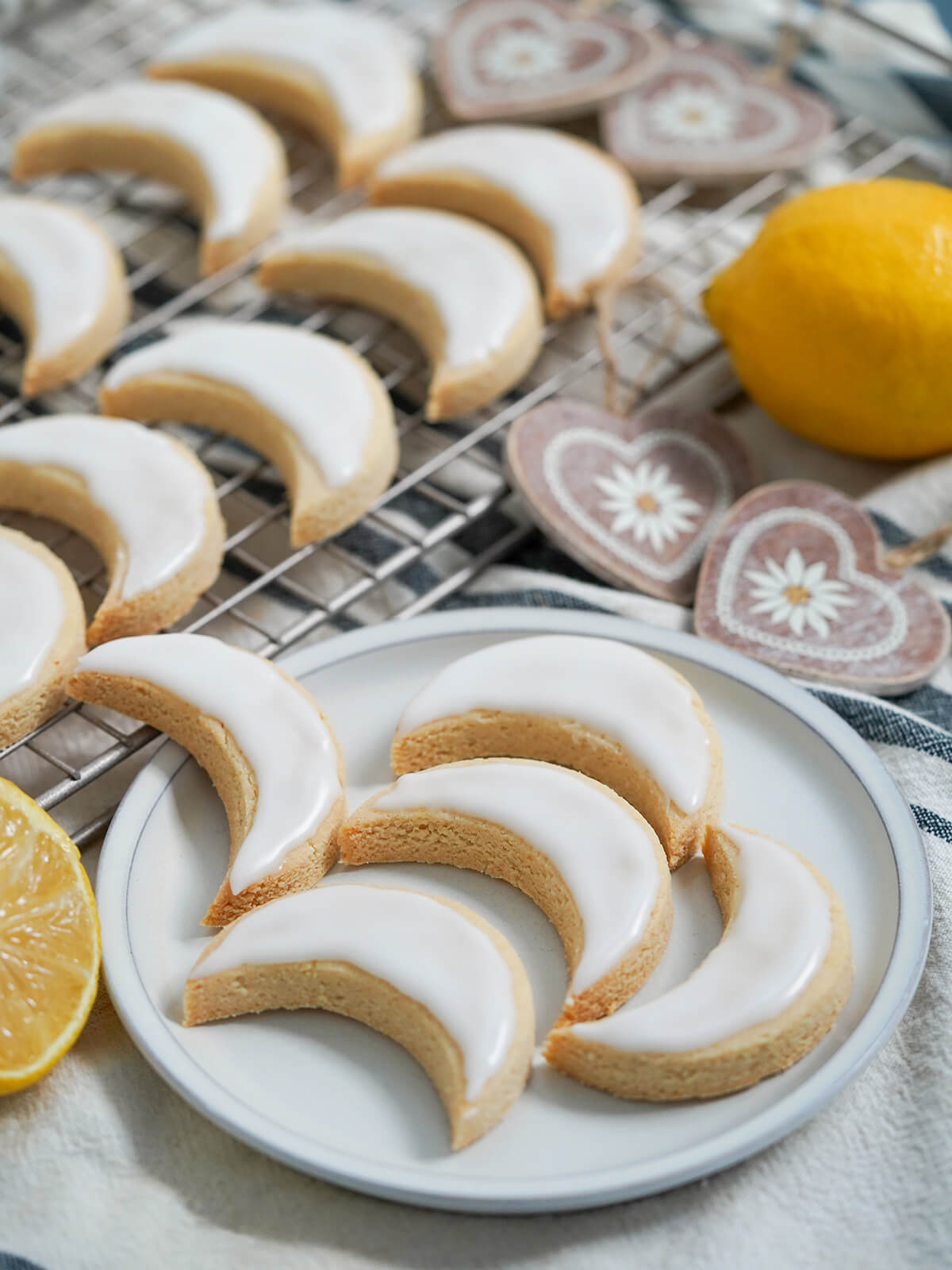 plate of lemon almond cookies zedernbrot with more on cooling rack behind and wood decorations and lemons around.