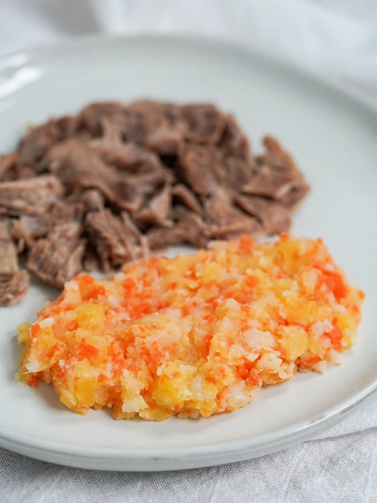 Swedish root vegetable mash, rotmos, served on plate with meat behind.