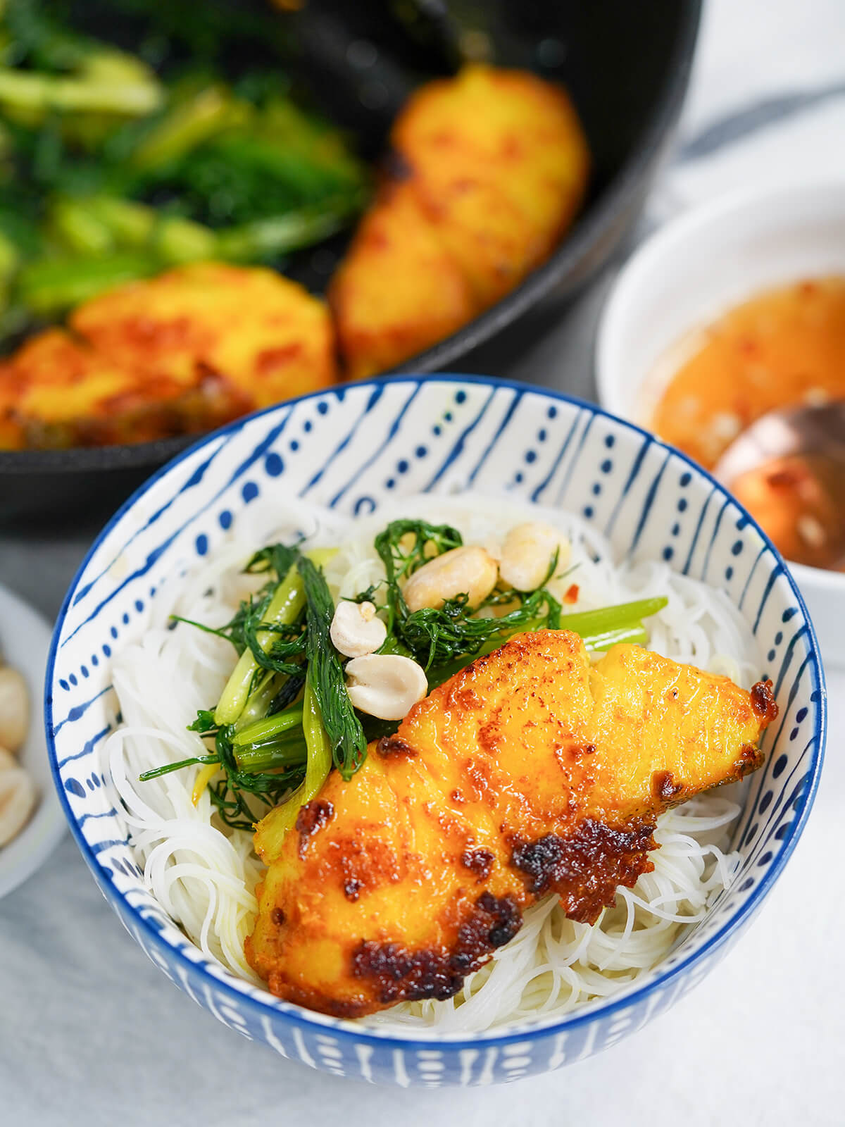 bowl of noodles topped with Vietnamese turmeric fish, cha ca la vong with cooked dill and skallion and peanuts on top.