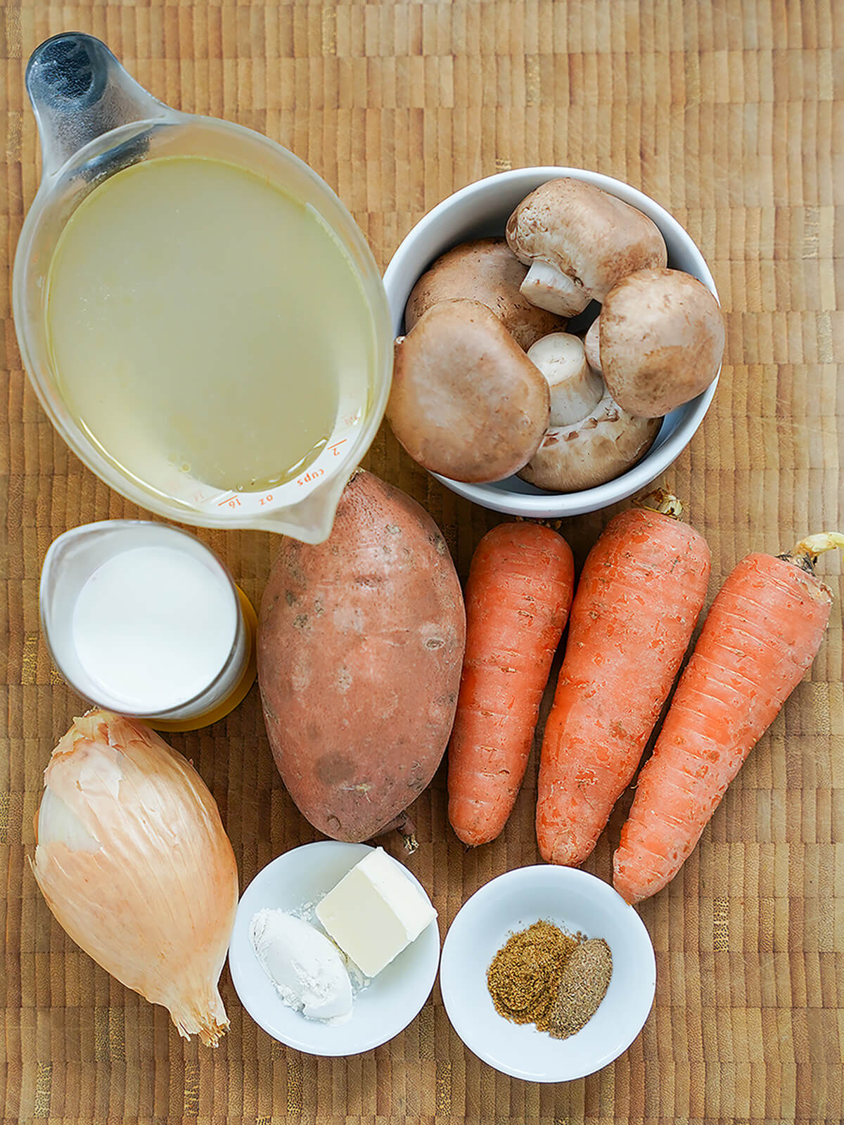 bowl of mushrooms, onion, sweet potato, carrots and measures with stock and milk, plus small dishes with spices, butter and flour.