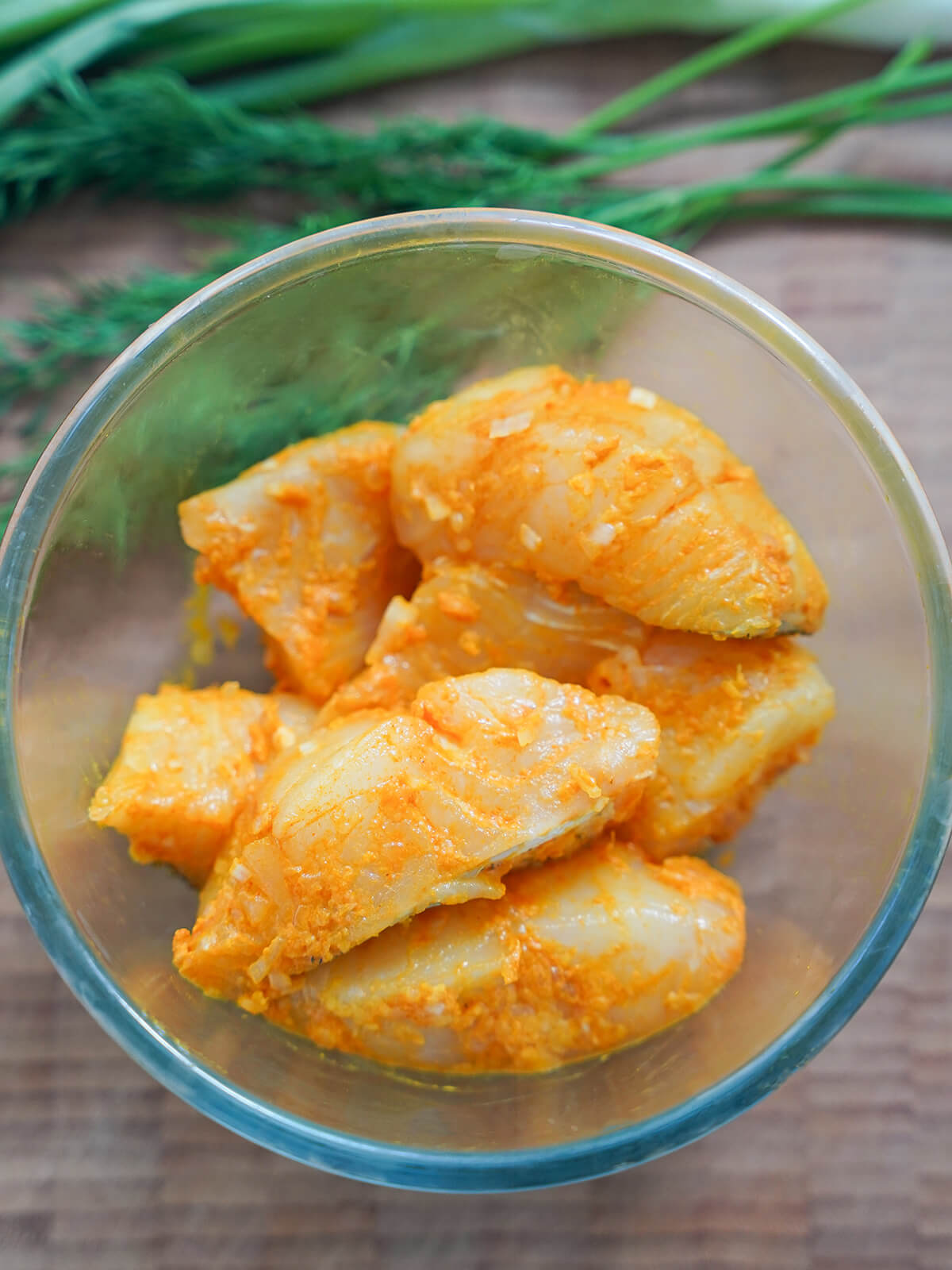 small bowl with pieces of yellow-orange fish coated in turmeric and spice marinade.