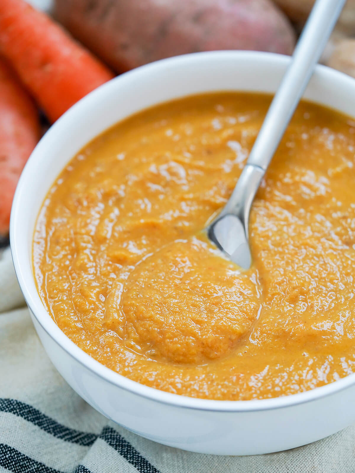 part view of bowl of mushroom carrot and sweet potato soup with spoon resting in bowl.