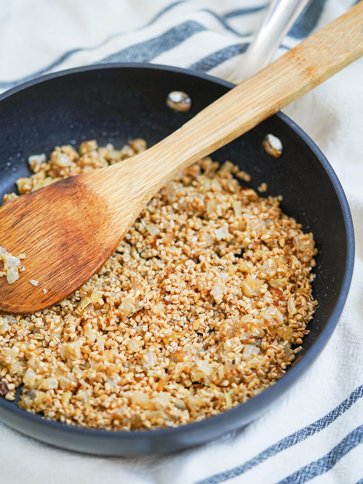 skillet of skirlie oatmeal stuffing with wooden spoon on top from side.