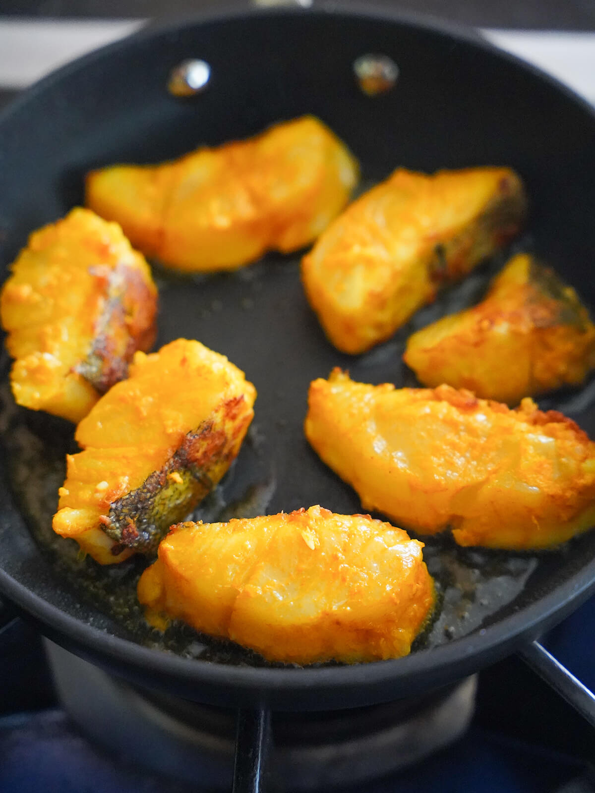 pieces of fish cooking in oil in a skillet, with a little browning on one side.