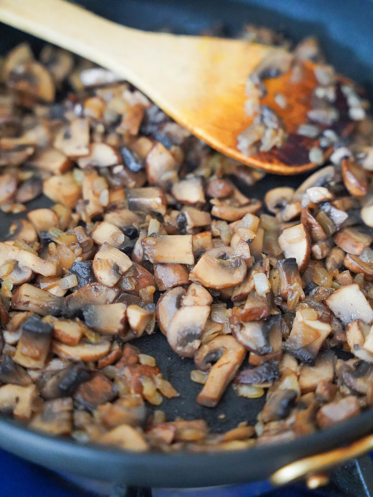 cooked down mmushrooms before adding liquid mushroom stroganoff cooked mushrooms and onions in skillet with wooden spatula resting on top.