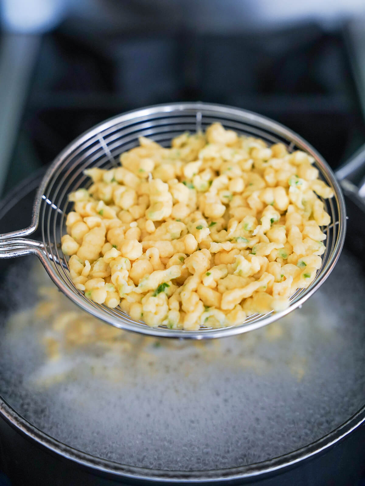 removing spaetzle from pot with slotted spoon straining spoon lifting spaetzle above pot of boiling water.