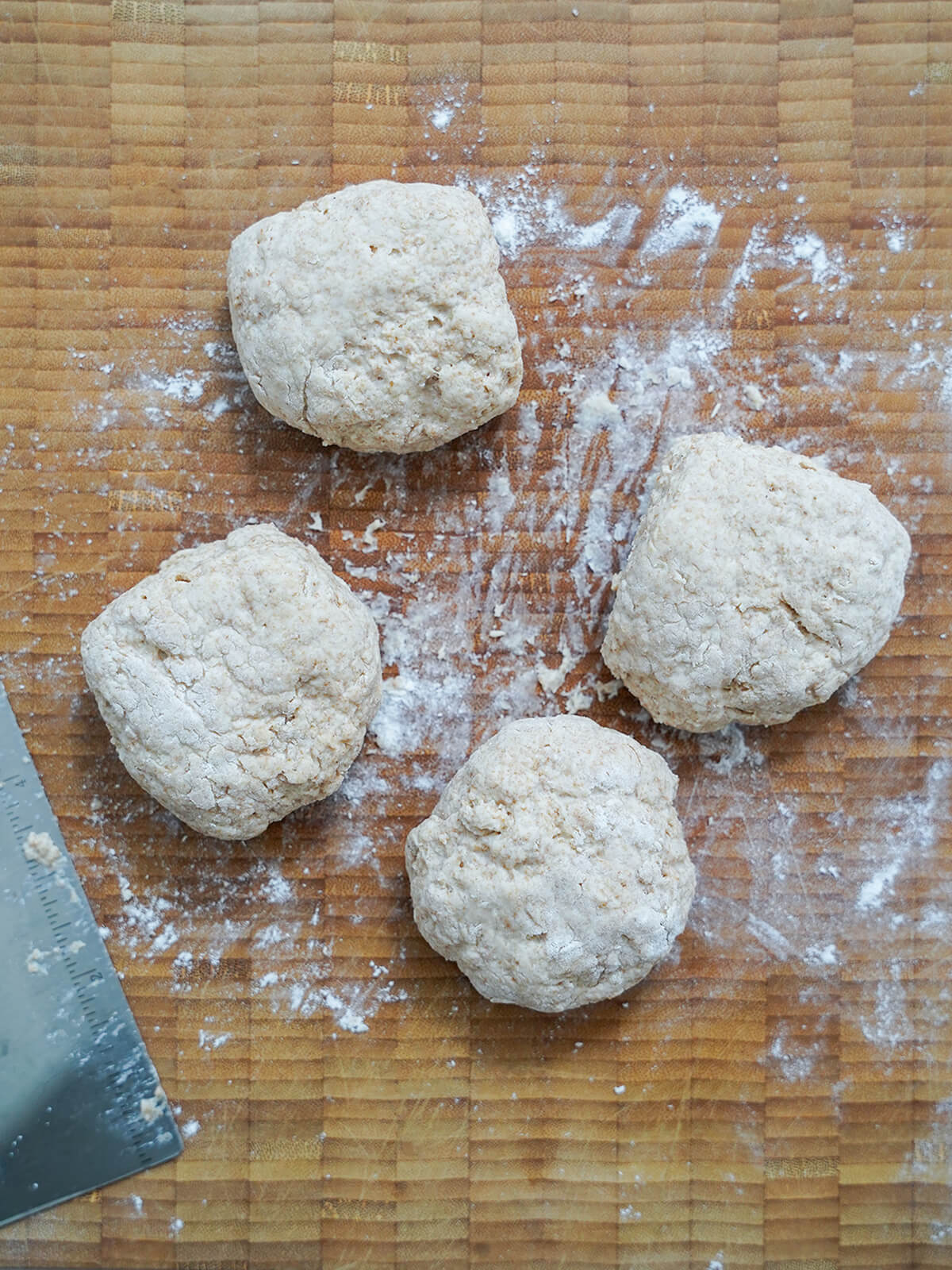 forming rolls on wooden board with dough cutter in edge of view.