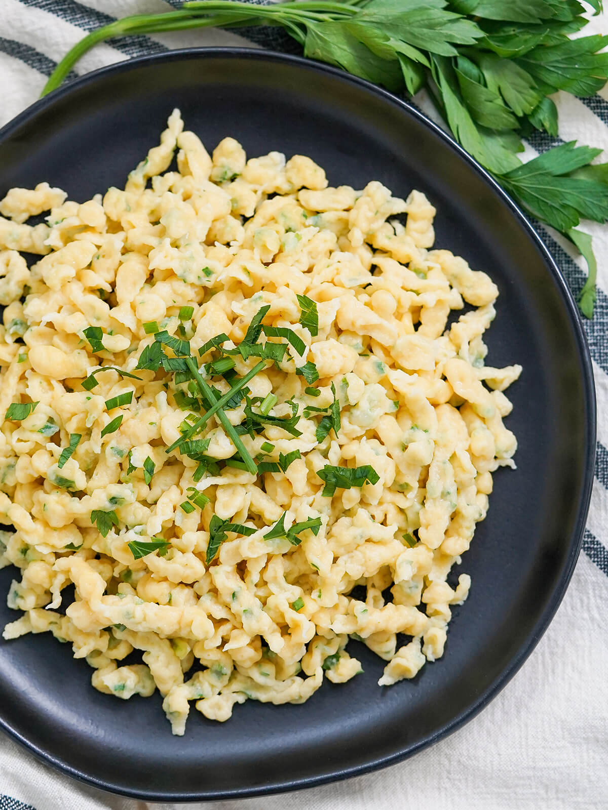 Herb spaetzle are easy to make and tasty both as a side or on their own with butter and herbs & optionally cheese. Comfort food, for sure! overhead close view of plate of herb spaetzle.