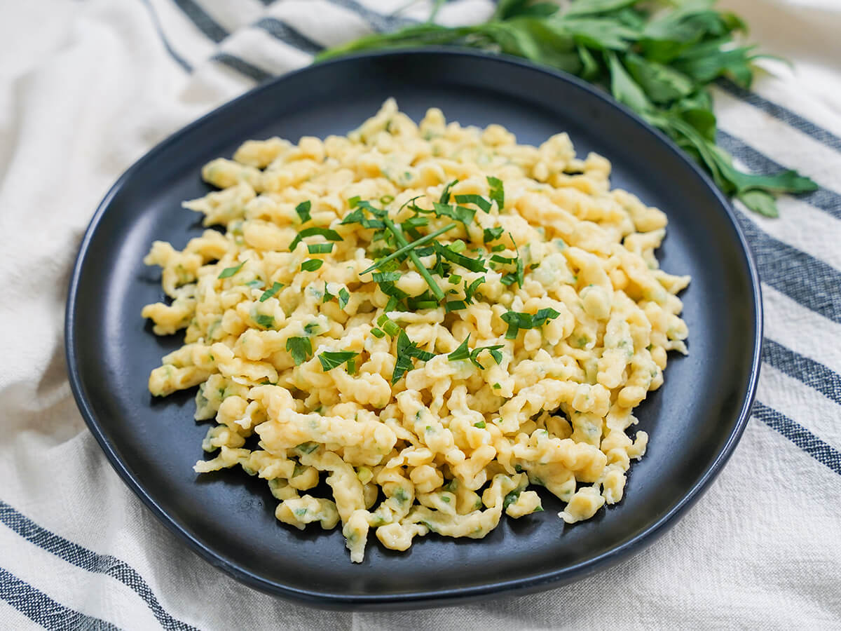plate of herb spaetzle side view of plate of herb spaetzle with herbs behind.