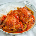 close view of plate of Basque chicken served with rice in back of plate.