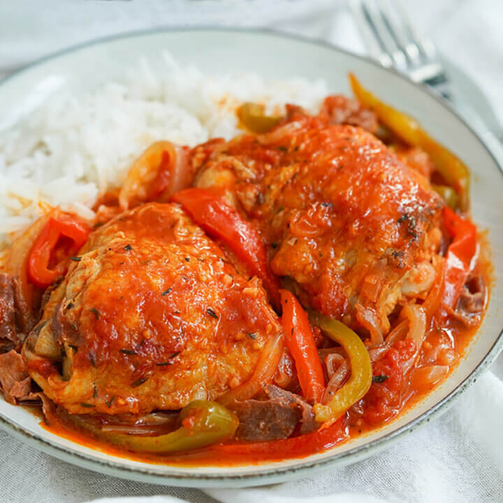 close view of plate of Basque chicken served with rice in back of plate.