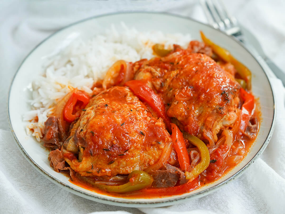 plate of Basque chicken with rice towards back of plate and fork in background.