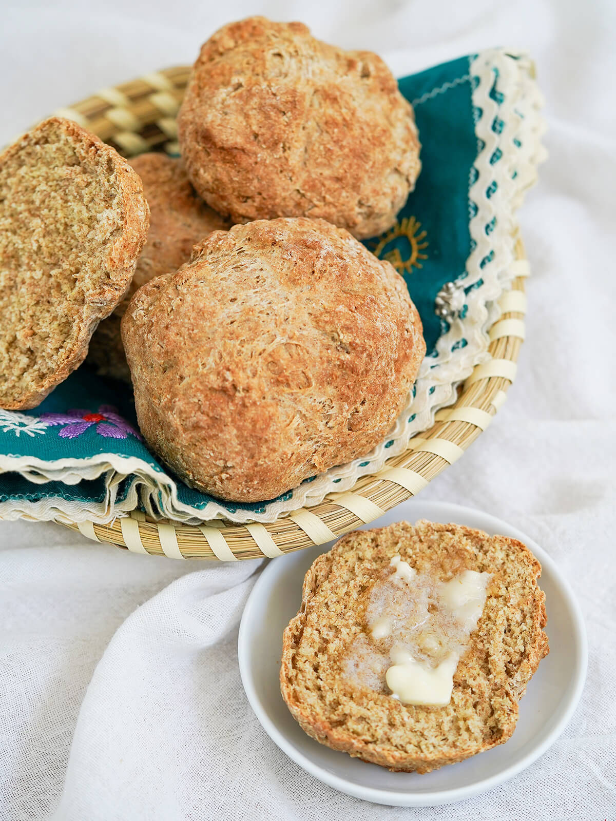 Irish soda bread rolls in a basket with half a roll on small plate in front topped with butter that is melting.