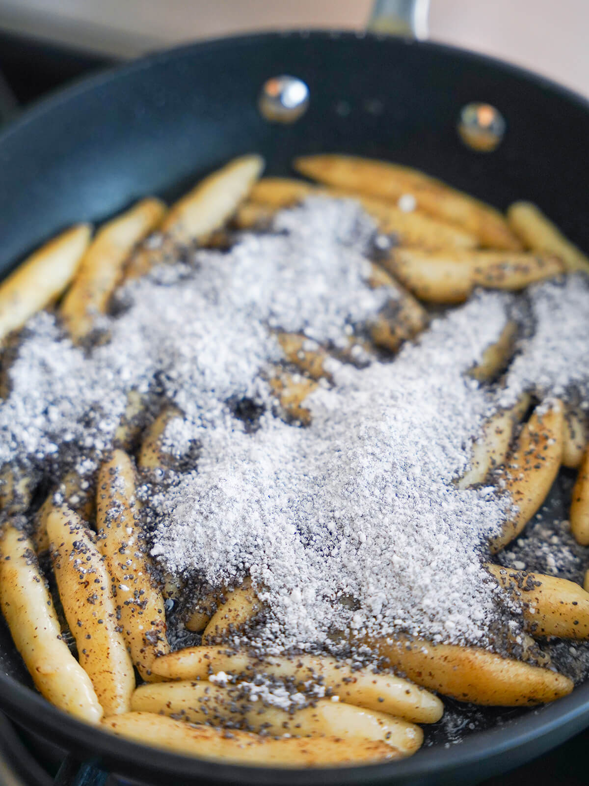 adding poppy seed and powdered sugar mixture over potato noodles in skillet.