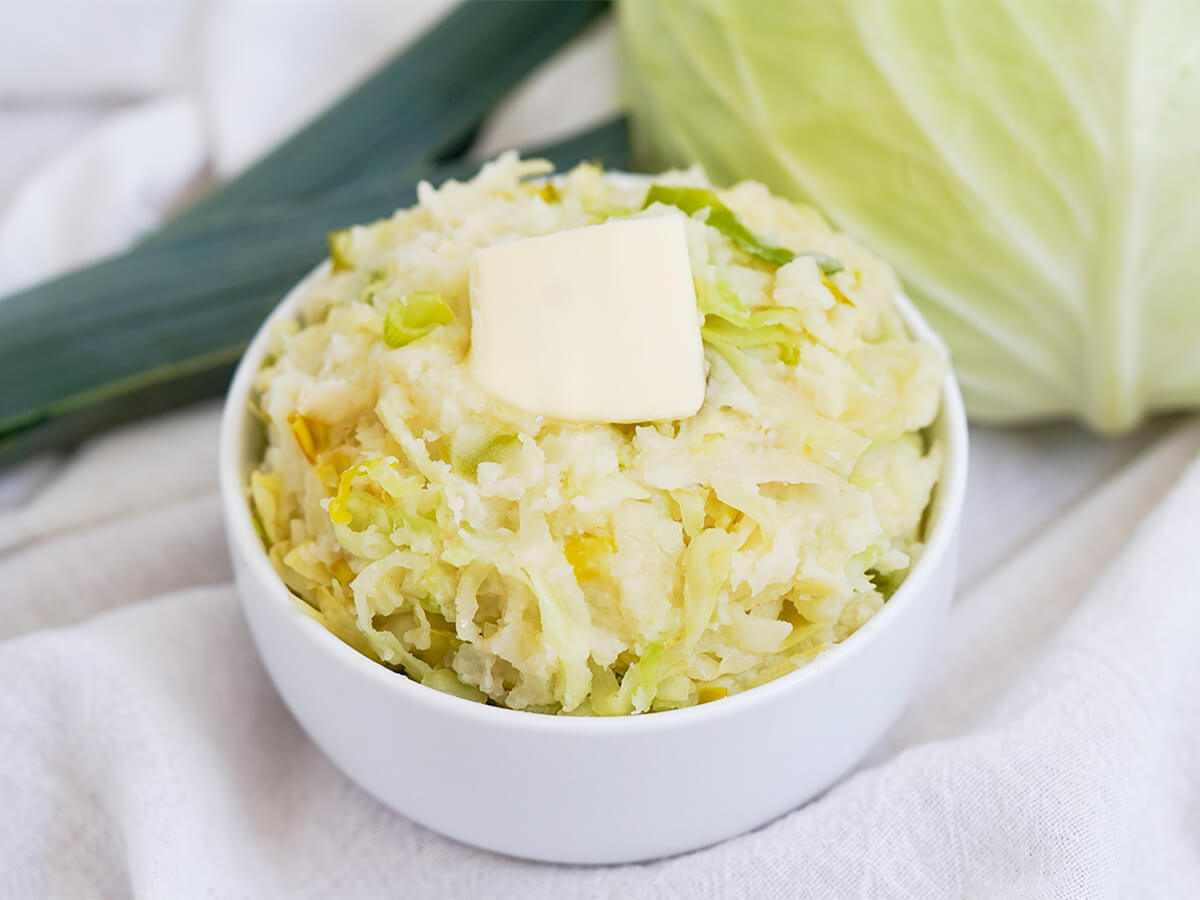 bowl of colcannon, mashed potatoes with cabbage, with part cabbage and leek behind.