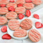 small plate with some strawberry shortbread cookies on it with one resting on side, more behind and pieces of dried strawberry around.