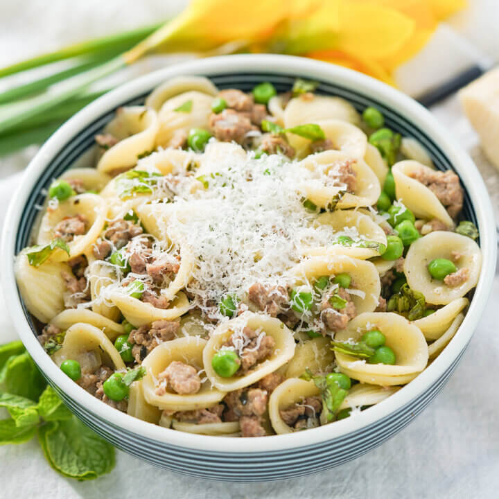 bowl of pea and lamb pasta topped with some grated cheese.