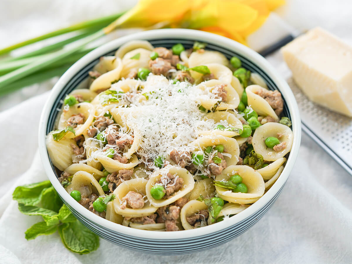 bowl of pea and lamb pasta bowl of pea and lamb pasta topped with cheese with block of cheese on grater behind.
