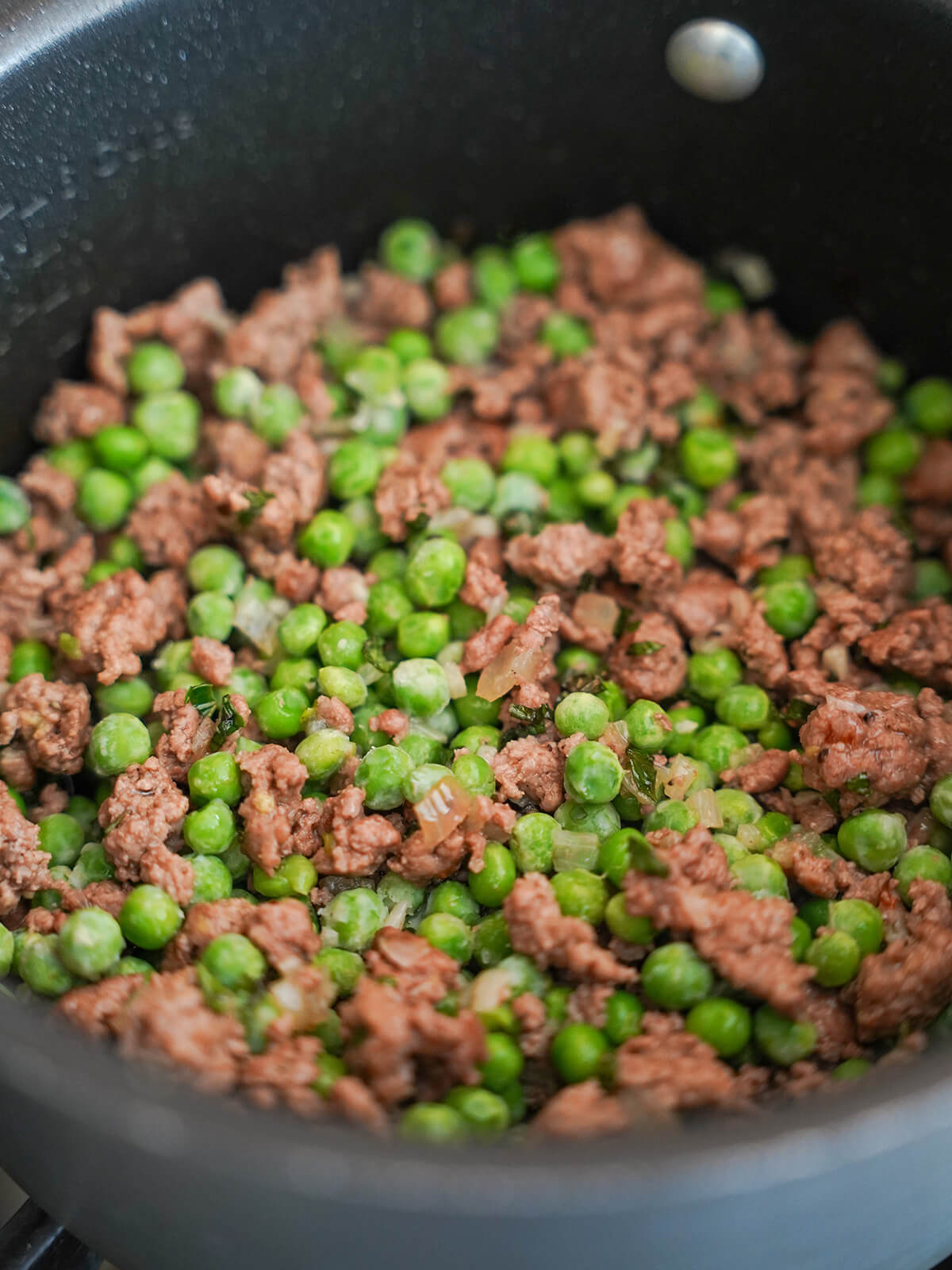 making the sauce for pea and lamb pasta peas and ground lamb mixture in pot.