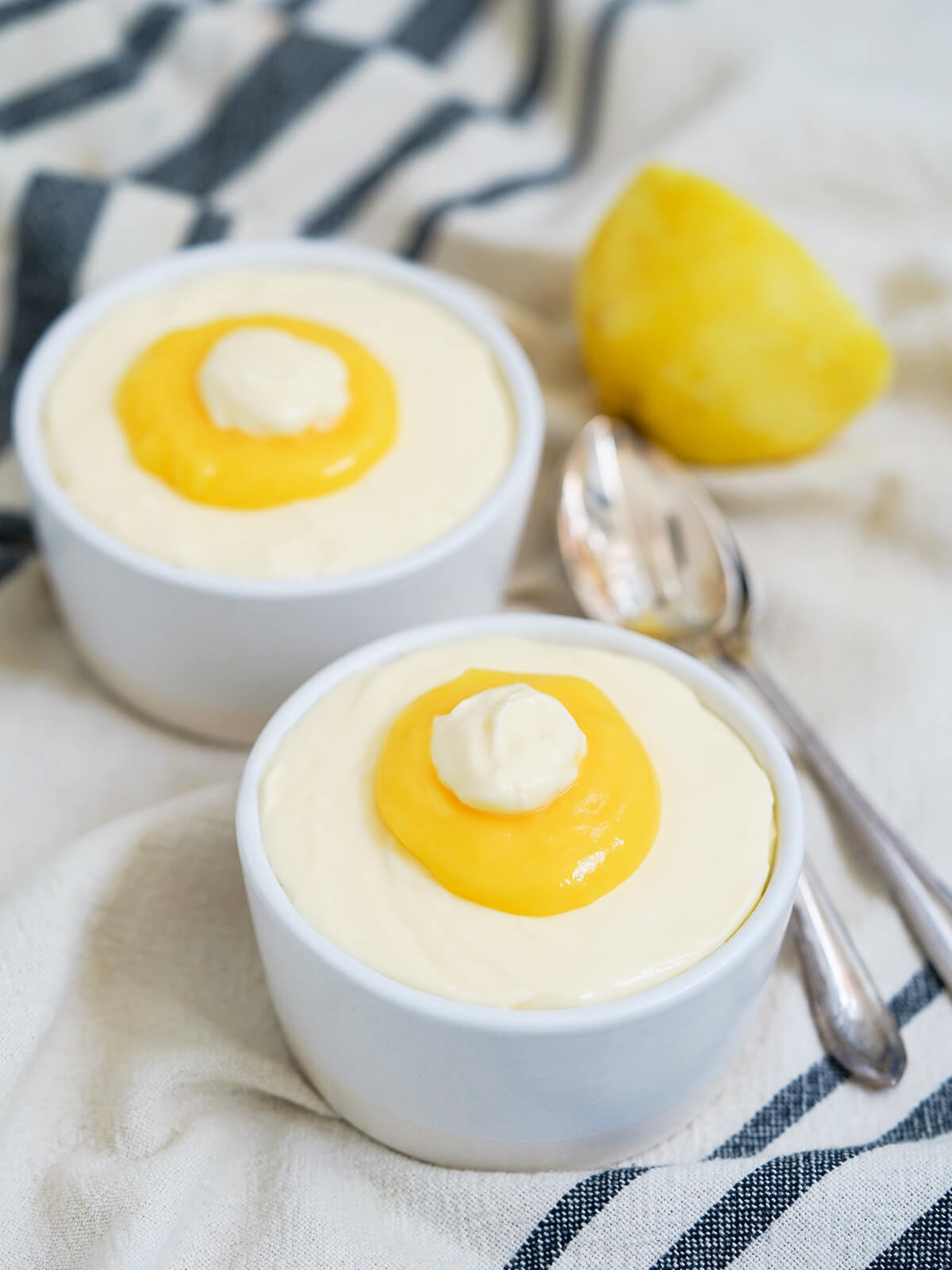 two dishes of lemon mousse with spoons behind front dish and part lemon behind.