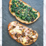 two llescas Catalan loaded toasts above each other, one with spinach topping other with ham, cheese and mushrooms.