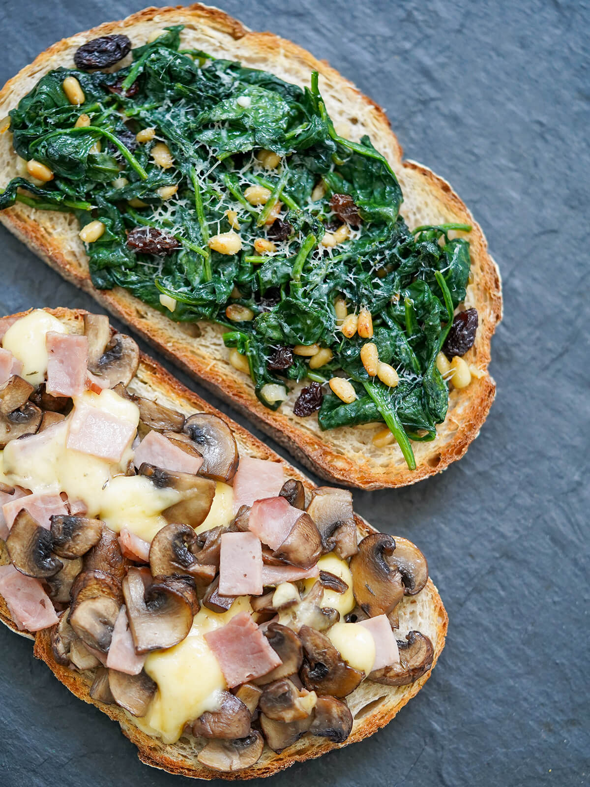 overhead part view of two llescas, Catalan loaded toasts, one topped with spinach other ham, mushroom and cheese.