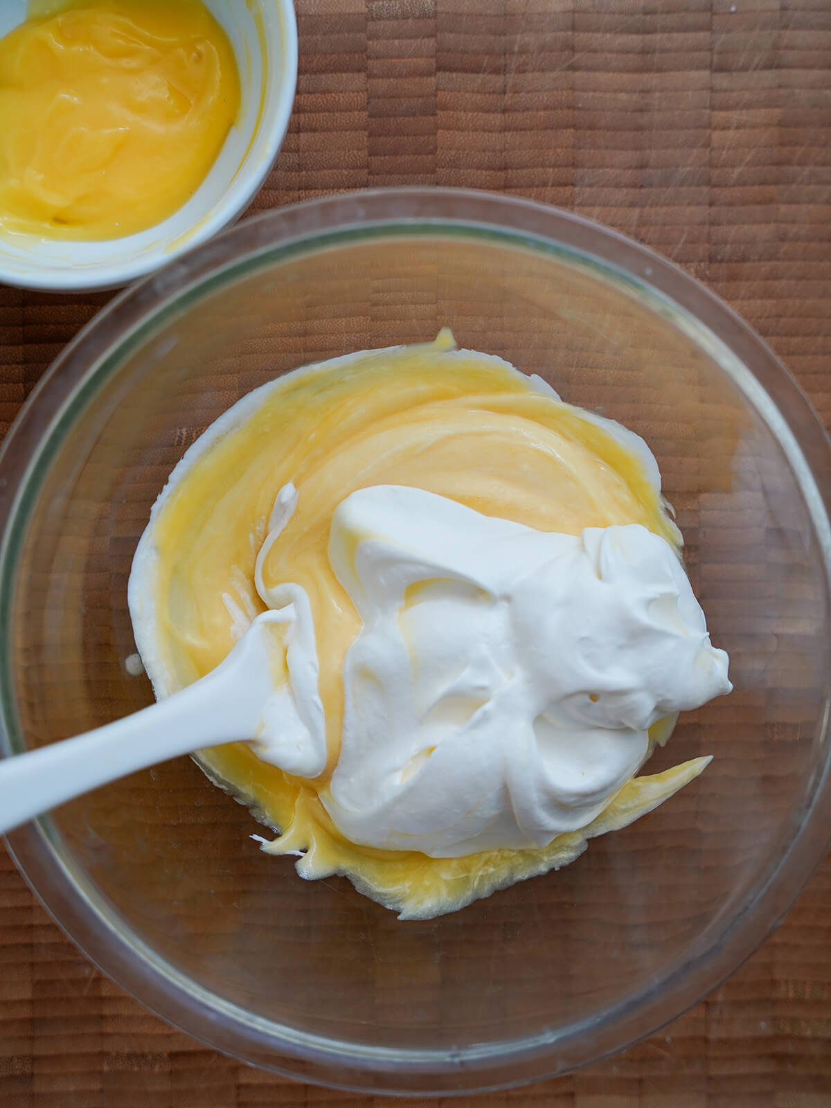 whipped cream on top of lemon curd mixture that has had a little cream mixed in with a little reserved lemon curd in dish above.