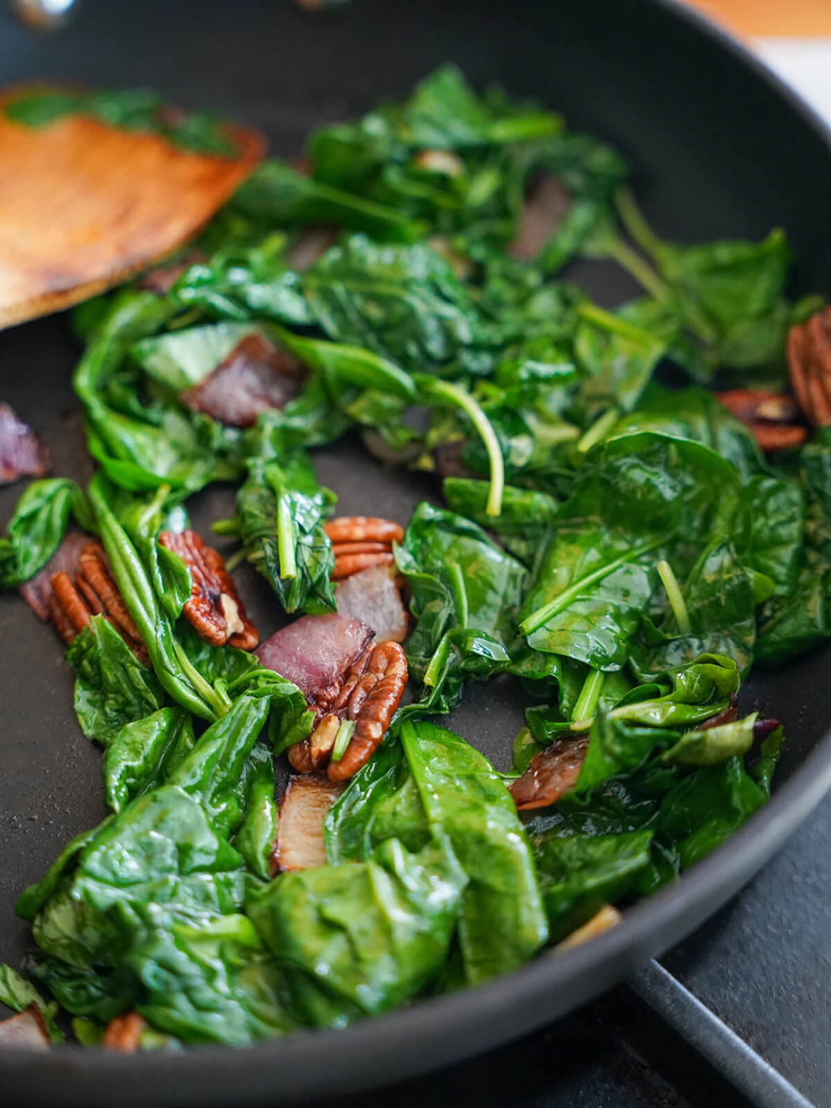 wilting greens and cooking onion for Peruvian pesto, tallarines verdes wilting spinach and basil in skillet with pecans, onion.