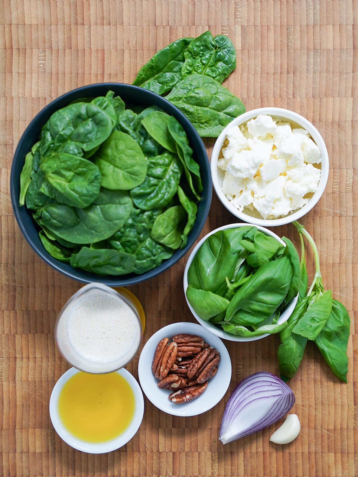 ingredients for Peruvian pesto for tallarines verdes. bowls of spinach, cheese, basil, pecans and measure of evaporated milk, oil, part of an onion and garlic clove.