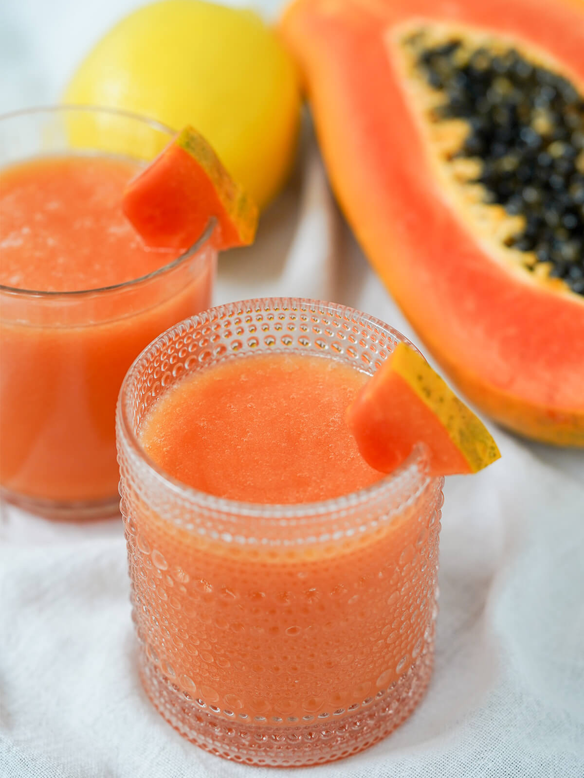 glass of papaya lemonade with part view of another glass and papaya in background.