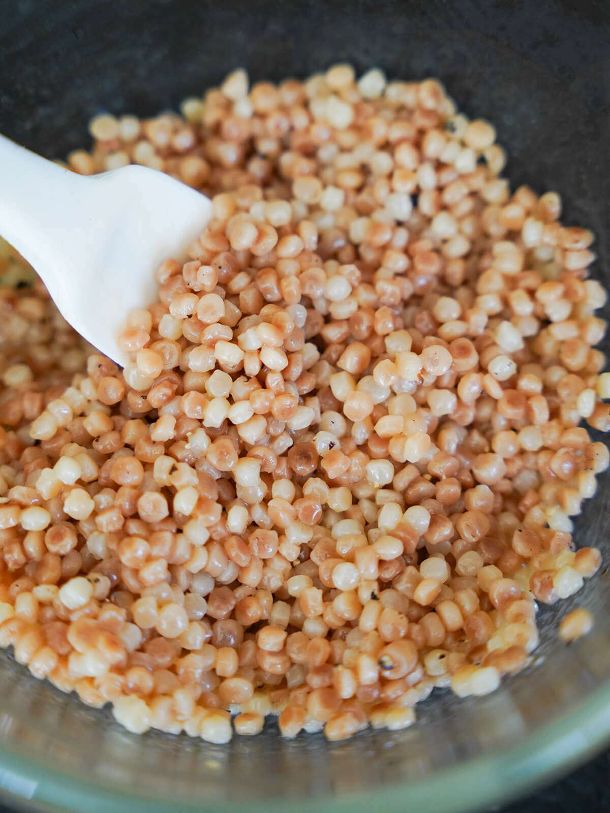 adding dressing to cooked pearl couscous