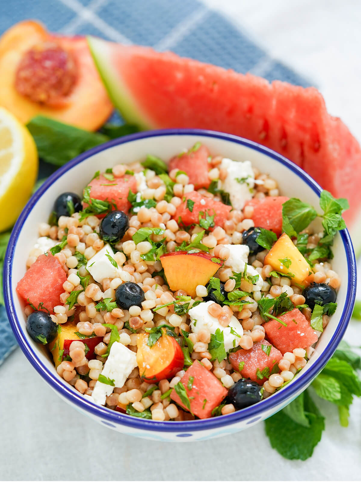 bowl of fruit couscous salad with wedge of watermelon and cut nectarine behind bowl.