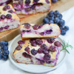slices of Schiacciata all’uva grape focaccia on plate with grapes behind.