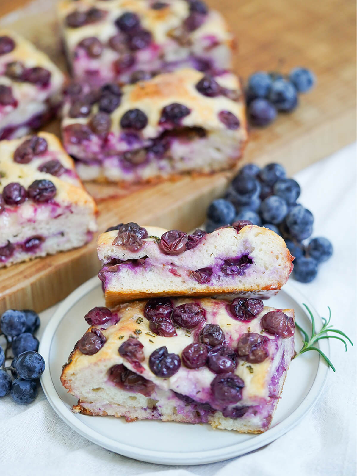 slices of Schiacciata all’uva grape focaccia on plate with grapes and more slices on board behind.